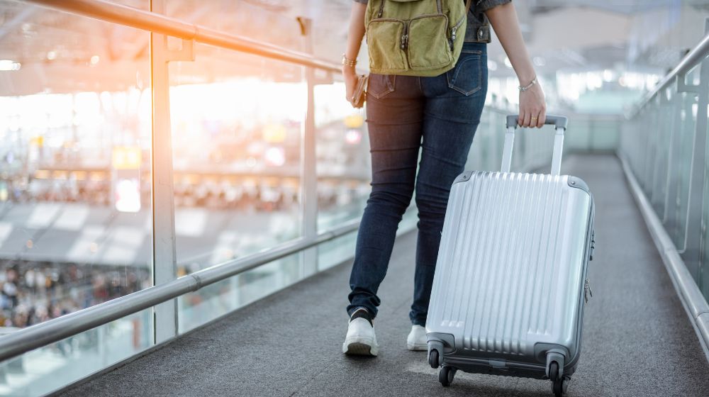 空港で軽量スーツケースを引く旅行者の後ろ姿。キャリーバッグを使った国内外旅行のイメージ。持ち運びやすく移動に便利な機内持ち込みサイズのスーツケース。